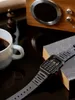 A vintage calculator watch is placed on a book next to a cup of coffee and a chess piece, with a wooden speaker in the background. Produktbild-Vorschau