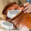 A person's hands are holding open a brown leather bag, revealing two white ultrasonic cleaners inside. Voir les images du produit