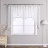 A white voile curtain with a scalloped edge and satin trim hangs in front of a window. A white floor lamp stands to the right, and a small cream-colored nightstand with two drawers is to the left. Produktbild-Vorschau