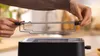 A person is holding a toaster rack over a toaster. Voir les images du produit
