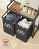 A close-up view of a two-tiered laundry hamper with two 46L baskets, one filled with clothes and the other with towels. A wooden shelf above holds decorative items. Produktbild-Vorschau