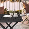 A small black folding table with a book, a potted plant, and a cup of coffee on it, placed on a balcony with a railing and water in the background. Anteprima dell’immagine prodotto