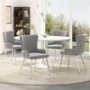 A dining set with four gray velvet chairs around a white round table, set in a well-lit room with a large window overlooking a garden. Podgląd zdjęcia produktu