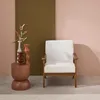 A white armchair with wooden legs sits next to a small brown side table with decorative vases and a plant. Anteprima dell’immagine prodotto