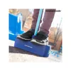 A child's feet are shown standing on a blue pogo stick base, with a blue pole extending upwards. The child is wearing sneakers and dark pants. The background appears to be an outdoor playground setting with other blue playground equipment visible. Produktbild-Vorschau