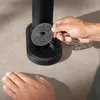 A person's hands are shown interacting with a black appliance, possibly a water carbonator, by holding a small, perforated metal disc over an opening. Produktbild-Vorschau