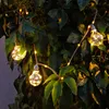 A string of decorative LED lights shaped like vintage light bulbs are draped over green foliage. Produktbild-Vorschau