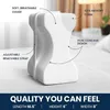 A white orthopedic knee pillow with labels pointing out its features, placed on a bed. Produktbild-Vorschau