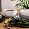 A collection of ceramic bowls and plates on a wooden table, with lime slices, peppercorns, and chives as garnish. Náhled obrázku produktu