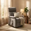 A gray recliner chair with a throw pillow and blanket is placed next to a window with sheer curtains. A side table with a lamp and plant is next to the chair. Produktbild-Vorschau