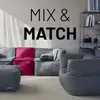 A modular sofa set with beanbag-style seating in gray and a pink corner piece, displayed in a living room setting with a shelf unit in the background. Voir les images du produit