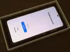 A smartphone is shown inside its packaging, displaying a welcome screen. Produktbild-Vorschau
