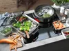 A WMF Aroma Vitalis steam cooker is shown on a modern induction stovetop, with various vegetables and ingredients prepared for cooking. Náhľad obrázku produktu