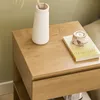 A close-up view of a wooden nightstand with a vase and a book on top. Produktbild-Vorschau