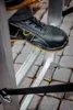 A close-up view of a person's foot wearing a black safety shoe stepping onto a silver ladder rung. Náhľad obrázku produktu