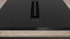 A close-up, top-down view of a black induction cooktop with a built-in ventilation system. Produktbild-Vorschau