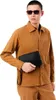 A man wearing a brown jacket and pants holds a black clutch bag. Produktbild-Vorschau