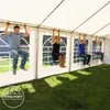 Four people hanging from the frame of a white party tent in a grassy outdoor area. Voir les images du produit