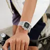 A person's arm wearing a clear digital watch, holding onto a bicycle handlebar. Produktbild-Vorschau