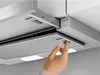 A close-up shot of a person's hand operating a control panel on a kitchen range hood. Voir les images du produit