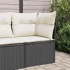 A close-up view of a black poly rattan corner sofa with cream cushions, placed on a paved patio next to green foliage. Podgląd zdjęcia produktu