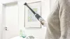 A person is using a vacuum cleaner attachment to clean a picture frame on a wall. Produktbild-Vorschau
