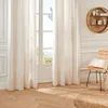 A bright room with large white curtains covering a window, a wicker chair with a striped cushion, and a round jute rug on a herringbone wooden floor. Produktbild-Vorschau