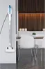 A white stick vacuum cleaner is mounted on a wall in a modern kitchen/dining area. Náhled obrázku produktu