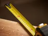 A close-up shot of a yellow measuring tape extended over a wooden surface. Voir les images du produit