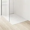 A close-up view of a modern white shower base with a glass shower wall and a silver drain. Produktbild-Vorschau