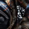 A close-up view of a dark fabric with a botanical pattern, showing folds and textures. Produktbild-Vorschau