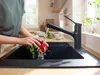 A person is washing radishes under a black kitchen faucet in a modern kitchen sink. Produktbild-Vorschau