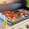 A grill with a griddle plate and a grill grate, both loaded with various vegetables being cooked. Produktbild-Vorschau