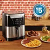 An air fryer is shown on a wooden countertop with food on plates in front of it. Voir les images du produit