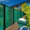 A green privacy screen is attached to a fence, with a house and trees in the background. A roll of the screen is shown in a circle in the lower right corner. Podgląd zdjęcia produktu
