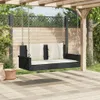 A black rattan swing bench with cream cushions hangs from a wooden pergola in a garden setting. Náhľad obrázku produktu