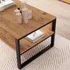 A close-up view of a rustic oak-effect coffee table with a black metal frame, featuring candles and books on its surface and shelf. Voir les images du produit