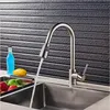 A kitchen faucet with water running into a sink, with fruit and a bottle in the background. Náhľad obrázku produktu