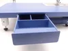 A close-up view of an open drawer on a blue sewing machine. Náhľad obrázku produktu