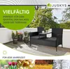 A black polyrattan garden bench with a table and cushions, placed on a wooden deck with potted plants. The background shows trees and a balcony railing. The image includes marketing text and seasonal imagery at the bottom. Náhľad obrázku produktu