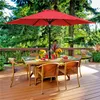 A red patio umbrella shades a glass-topped dining table with wicker chairs on a wooden deck, surrounded by lush greenery. Produktbild-Vorschau