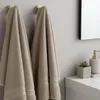 Two beige towels hanging on gold hooks in a bathroom. Produktbild-Vorschau