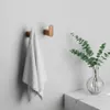 A bathroom scene with two copper hooks on a white wall, one holding a white towel, and a vase with eucalyptus on a marble countertop. Produktbild-Vorschau