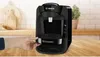 A black Bosch Tassimo coffee machine is shown on a wooden countertop with a hand reaching to adjust the drip tray. The background includes a tiled wall and a plant. Náhľad obrázku produktu