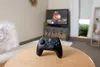 A black Nintendo Switch controller sits on a wooden table in front of a television displaying Mario. Anteprima dell’immagine prodotto