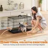 A woman is interacting with a small dog next to a black metal dog crate. Podgląd zdjęcia produktu