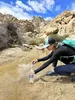 A person is filtering water from a stream in a rocky, desert-like environment. Podgląd zdjęcia produktu