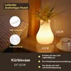 A bedside table with a glowing vase lamp and decorative flowers. Produktbild-Vorschau