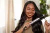 A woman is using a hair straightener on her long, dark hair. Voir les images du produit