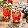 Two glasses of strawberry drinks with ice and mint on a wooden table, with bar tools and strawberries in the background. Náhled obrázku produktu